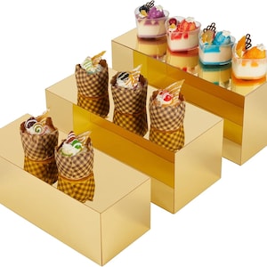 Puede incluir: Una variedad de postres en miniatura, incluyendo parfaits y cupcakes en capas, se exhiben en tres plataformas rectangulares de color dorado. Los postres presentan coloridas coberturas y están dispuestos en una presentación escalonada, creando una disposición visualmente atractiva.