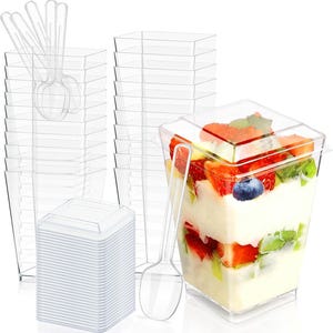Puede incluir: Vasos de postre de plástico transparente con tapas y cucharas. Una taza está llena de postre en capas, que incluye fresas, kiwi y arándanos. Las tazas son cuadradas y están apiladas.