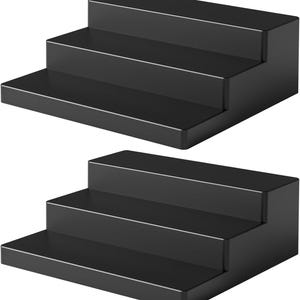 May include: Two black, three-tiered display stands. Each stand has three rectangular steps, creating a staircase effect. The stands are made of a solid, matte black material, suitable for showcasing small items.