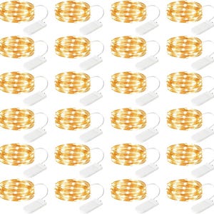 May include: A collection of warm white LED string lights, each coiled and connected to a small white battery pack. The lights are arranged in a grid pattern, creating a bright and festive display. Ideal for decorative purposes.