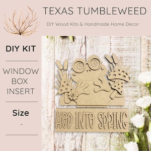 May include: A wooden DIY window box insert featuring a frog wearing glasses, mushrooms, and the phrase "Hop Into Spring." The product is from Texas Tumbleweed, a DIY wood kit and handmade home decor brand.