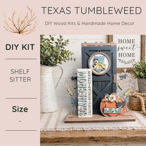 May include: A DIY wood kit shelf sitter featuring a dark gray door, a vertical sign reading SCARECROW CROWS BURLAP STRAW, and an orange pumpkin cutout with the text Hello Fall. The set includes a scarecrow face, corn stalks, and a bird.