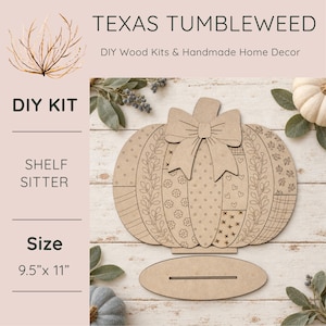 May include: A laser-cut wooden pumpkin DIY kit with a bow topper and a separate oval base. The pumpkin features various engraved patterns including leaves, flowers, hearts, and cross-stitches. The text reads Texas Tumbleweed, DIY Wood Kits & Handmade Home Decor, DIY Kit, Shelf Sitter, and Size 9.5" x 11".