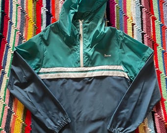 May include: A teal and navy blue hooded windbreaker jacket with a white stripe across the chest. The jacket has a half-zip closure and the word "Run-ins" is printed on the chest. The jacket is displayed on a colorful, striped background.