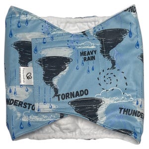 May include: A blue and white pet belly wrap featuring a weather-themed design with tornados, rain, and the words "Tornado", "Thunderstorm", and "Heavy Rain". The wrap has a white interior and a velcro closure.