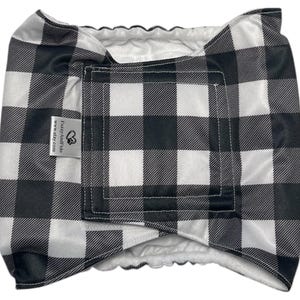 May include: A black and white buffalo plaid pet diaper with a white interior. The diaper has a rectangular shape with a hook and loop closure and a tag that reads "FuzzyAndToo" and "www.etsy.com".