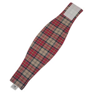 May include: A red, tan, and navy plaid heating pad wrap with a hook and loop closure. The wrap is approximately 20 inches long and 5 inches wide. The wrap has a tag with text.