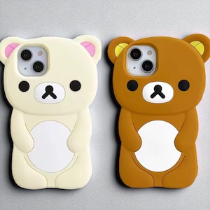 Op de afbeelding: Twee telefoonhoesjes in de vorm van cartoonberen. Eén is crème met roze accenten, de andere is bruin met gele accenten. Beide hebben zwarte ogen en een zwarte neus, ontworpen voor een smartphone.
