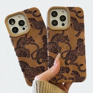 May include: Two brown phone cases with a leopard print design. The cases have a tan border around the camera and a repeating pattern of black leopard spots and outlines. The cases are held up in front of a light background.