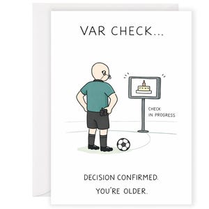 Peut inclure: Carte d'anniversaire avec une illustration de dessin animé d'un arbitre de football. Le texte "VAR CHECK..." est en haut, et "DECISION CONFIRMED. YOU'RE OLDER." en bas. L'arbitre est à côté d'un écran avec un gâteau.