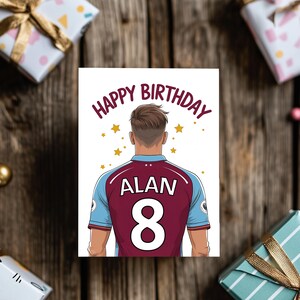 May include: A birthday card featuring a cartoon illustration of a soccer player wearing a maroon and blue jersey with the name "ALAN" and the number "8" on the back. The card has the text "HAPPY BIRTHDAY" in a circle around the player's head.