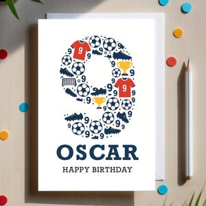 Op de afbeelding: Een witte verjaardagskaart met de naam "OSCAR" en "HAPPY BIRTHAY" in marineblauw. Het cijfer "9" is gevormd uit voetballen, schoenplaatjes, shirts en trofeeën. Kleurrijke confetti en een potlood liggen op het houten oppervlak.