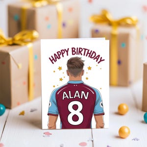 May include: A white card with the words "Happy Birthday" in black text. A cartoon illustration of a person wearing a maroon and blue soccer jersey with the name "Alan" and the number "8" on the back. The background is white with gold stars.