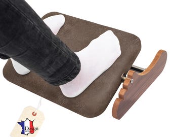 May include: A brown footrest with a wooden base and a padded top. The footrest is designed to provide comfort and support. The image shows a person's feet resting on the footrest. The tag says "Design en France".