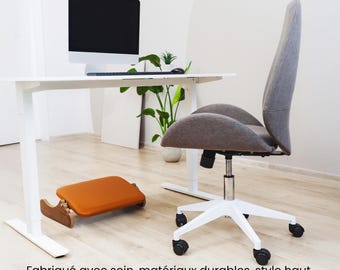 May include: A white desk with a computer monitor, a potted plant, and a gray office chair with a white base and black wheels. A brown footrest is in the foreground. The text "Améliorez votre espace de travail" is at the top of the image. The text "Fabriqué avec soin, matériaux durables, style haut de gamme" is at the bottom of the image.