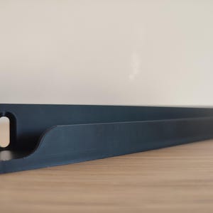 May include: A black, angled shelf with a curved front edge and a rectangular cutout on the left side. The shelf is made of a solid material and sits on a wooden surface. The shelf is designed to hold items.