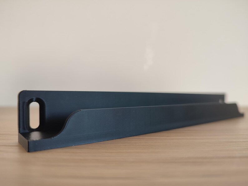 May include: A black, angled shelf with a curved front edge and a rectangular cutout on the left side. The shelf is made of a solid material and sits on a wooden surface. The shelf is designed to hold items.