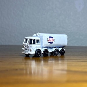 May include: White toy truck with a Pepsi-Cola logo on the side. The truck has four wheels and a white cab.