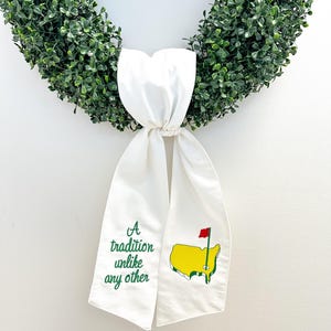 May include: A white fabric ribbon with green embroidery that reads "A tradition unlike any other" and a green and yellow embroidered image of the United States with a red flag. The ribbon is tied around a green wreath.