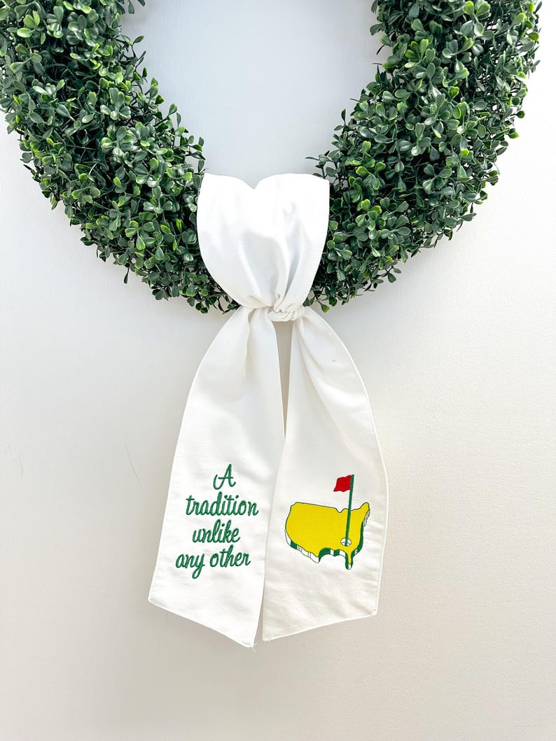 May include: A white fabric ribbon with green embroidery that reads "A tradition unlike any other" and a green and yellow embroidered image of the United States with a red flag. The ribbon is tied around a green wreath.
