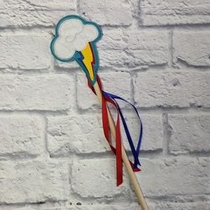 May include: A wooden wand with a blue and yellow lightning bolt and a white cloud on top. The wand has red and blue ribbons attached to it.