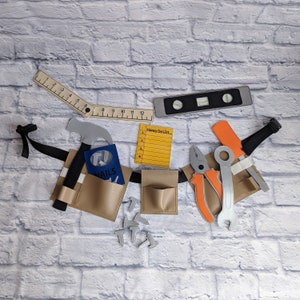 May include: A tan tool belt with a black strap, holding toy tools. Includes a hammer, wrench, pliers, level, ruler, and a notepad that says "Honey Do List". Also includes toy nails.