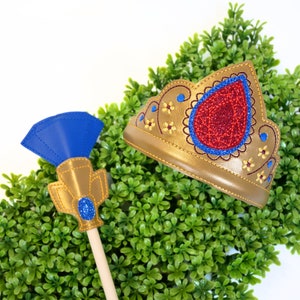 Puede incluir: Una corona dorada con una joya roja y bordados florales azules, y un cetro azul y dorado con una joya azul.