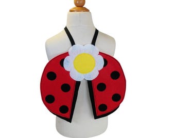 Puede incluir: Alas de disfraz de mariquita rojas y negras con una flor blanca con un centro amarillo. Las alas están unidas a una correa negra.