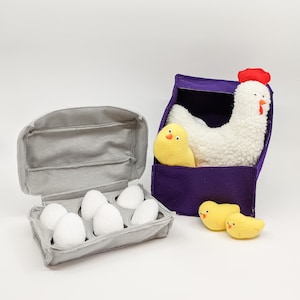 May include: A gray felt egg carton with six white felt eggs and a purple felt chicken coop with a white felt chicken and two yellow felt chicks.