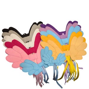 May include: A collection of felt wing accessories in various colours including black, grey, white, magenta, pink, light blue, orange, and yellow. Each set of wings features a central rectangular tab and long, dangling fabric ribbons at the base.