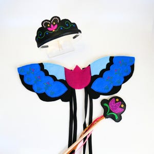 Op de afbeelding: Een blauw en zwart vlinderkostuum met roze accenten. Het kostuum bevat vleugels, een toverstaf en een kroon.