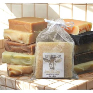 May include: A collection of handmade soaps in various colors, including brown, beige, and green. One soap is packaged in a clear bag with a label that reads "Beaver Ridge Soap". The soaps are stacked on a tiled surface.