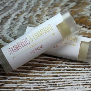 May include: Two clear lip balm tubes with white labels. The label on the top tube reads "Strawberries & Champagne Lip Balm". The label on the bottom tube reads "Champagne".