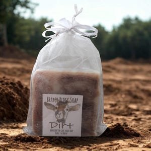 May include: A rectangular bar of soap inside a white sheer organza drawstring bag. The label features a goat illustration and the text: Brayer Ridge Soap, Dirt, Handcrafted Goat Milk Soap, What I'm Really.