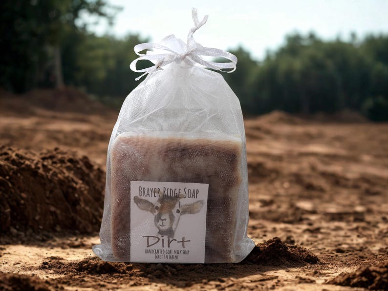 May include: A rectangular bar of soap inside a white sheer organza drawstring bag. The label features a goat illustration and the text: Brayer Ridge Soap, Dirt, Handcrafted Goat Milk Soap, What I'm Really.
