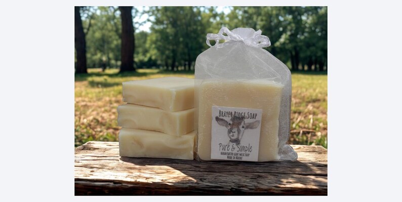 Puede incluir: Una pila de tres jabones rectangulares de color claro junto a una barra de jab&oacute;n m&aacute;s grande en una bolsa de malla. La bolsa tiene una etiqueta que dice "Beaver Ridge Soap" con una ilustraci&oacute;n de cabra y las palabras "Pure & Simple".