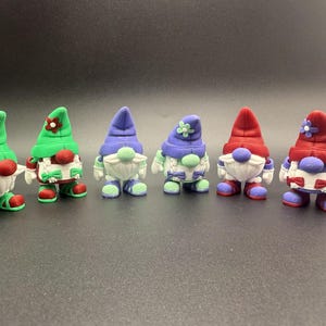 Puede incluir: Una colecci&oacute;n de seis figuras de gnomos coloridos. Cada gnomo tiene una barba blanca, una nariz redonda roja y un sombrero en varios colores, incluyendo verde, morado y rojo. Los gnomos visten zapatos y trajes a juego.