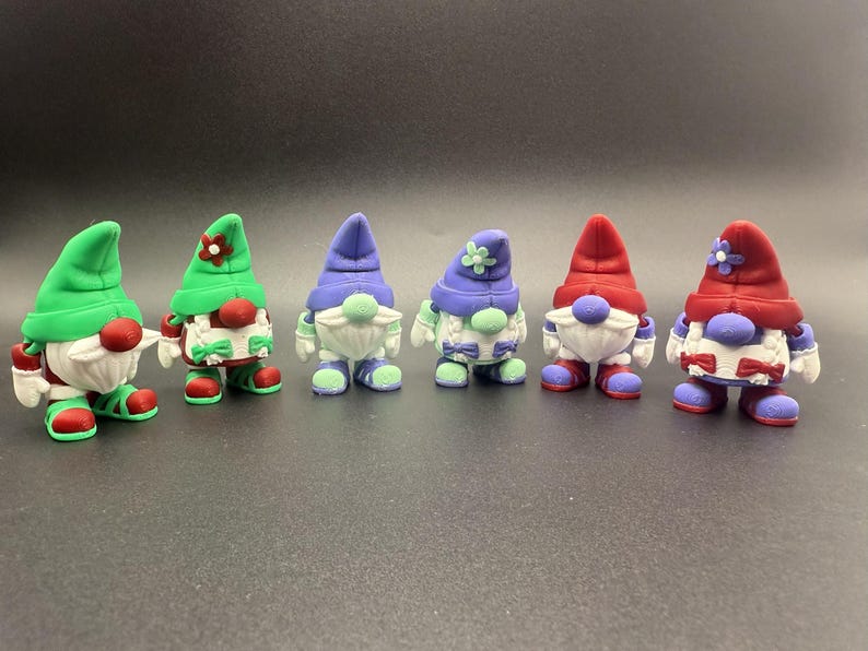 Puede incluir: Una colecci&oacute;n de seis figuras de gnomos coloridos. Cada gnomo tiene una barba blanca, una nariz redonda roja y un sombrero en varios colores, incluyendo verde, morado y rojo. Los gnomos visten zapatos y trajes a juego.