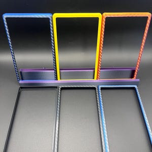 May include: A set of six rectangular frames in various colors. Three frames are upright, in blue, yellow, and orange, and three are flat, in black, gray, and blue. All frames have a textured pattern on the edges.