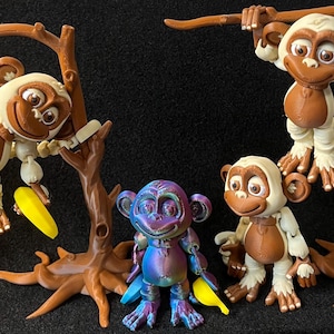 May include: Four articulated monkey figurines, three are brown with white fur and are hanging from brown tree branches. One monkey is blue and purple and is standing on the ground. The monkeys have large eyes and are smiling.