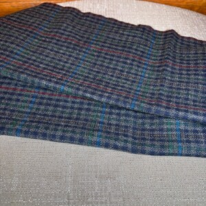 May include: A folded piece of fabric with a blue, green, and red plaid pattern. The fabric is a dark blue with a small checkered design. The plaid includes thin lines of red, green, and blue. The fabric is resting on a light grey surface.