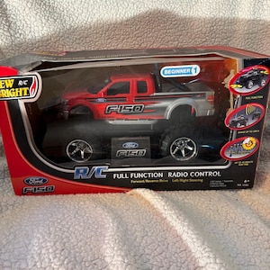May include: A red and silver Ford F-150 R/C truck in its original packaging. The box features the text "Ford F-150" and "Full Function Radio Control". The truck has large black tires and is labeled "Beginner".