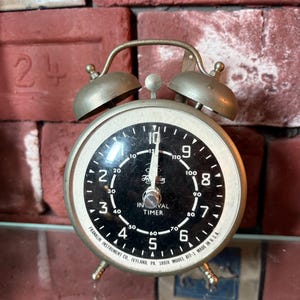 May include: Vintage Franklin Interval Timer with a black face, white numerals, and a silver metal casing. The timer has two bells on top and three small legs. The text "Franklin Instrument Co." is visible.