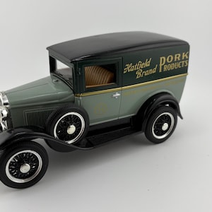 May include: A die-cast model of a vintage delivery truck. The truck is painted in shades of green and black, with the text "Hatfield Brand Products" on the side. The wheels are black with silver accents.
