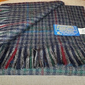 May include: A navy, grey, red, and green plaid wool scarf with a fringed edge. The scarf has a blue tag that reads "Pendleton" and "Pure Virgin Wool Made in U.S.A."