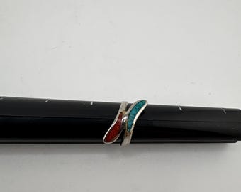 May include: A silver ring with a unique design. The ring features two curved inlays, one red and one turquoise. The ring is displayed on a black ring sizer against a white background. The ring's design is modern and eye-catching.