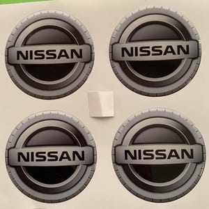 May include: Four silver and black car hubcaps with the word "NISSAN" in white lettering.