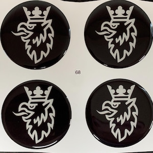 Könnte beinhalten: Vier schwarze, kreisförmige Embleme mit einem weißen Greif-Design, jeweils mit einer Krone. Die glänzenden Embleme scheinen Aufkleber oder Abziehbilder zu sein. Die Zahl "68" ist weiß zwischen zwei der Embleme gedruckt.