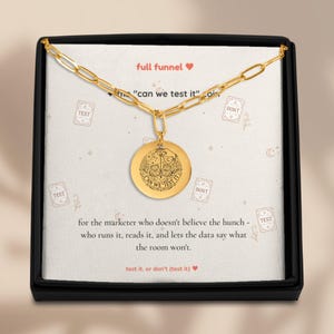 Könnte beinhalten: Eine goldfarbene Kettenhalskette mit einem runden Anhänger, der eine Hand mit zwei Karten und den Text "CAN WE TEST IT" zeigt. Die Kette liegt auf einer weißen Karte mit dem Text "full funnel" und "test it. or don't (test it)".