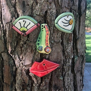 Four pieces which represent a Picasso-Style goofy tree face are placed on a pine tree trunk - two colorful eyes, a nose, and bright red lips.